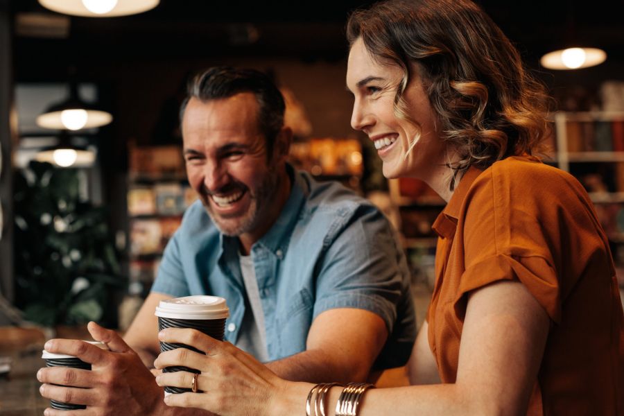 Two people smiling and holding coffee cups while sitting together in a cozy café.