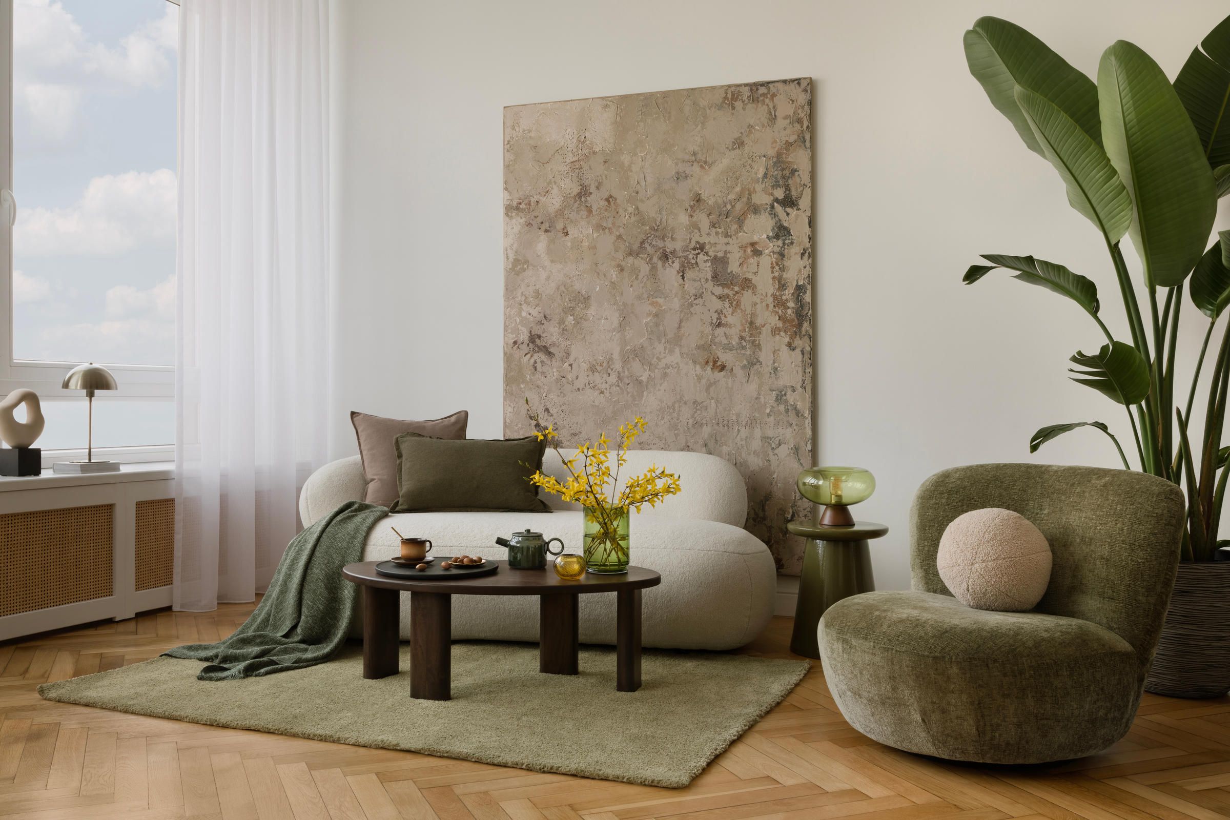 Modern living room with neutral furniture, green accents, large plant, and textured wall art above a cozy rug.