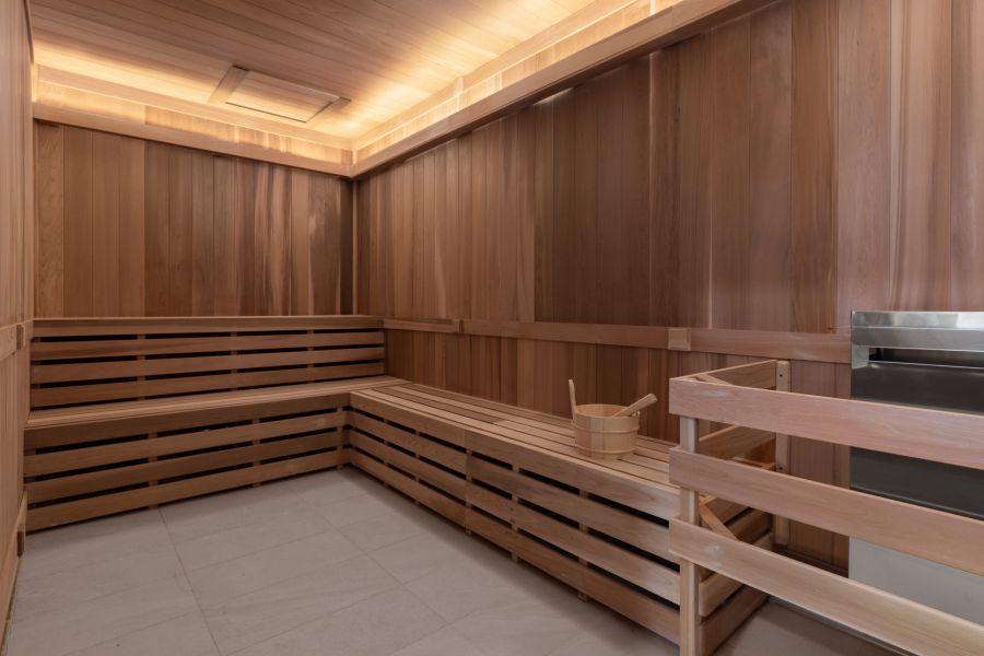 Wooden sauna room with built-in benches, a bucket with a ladle, and a heater on the right side.