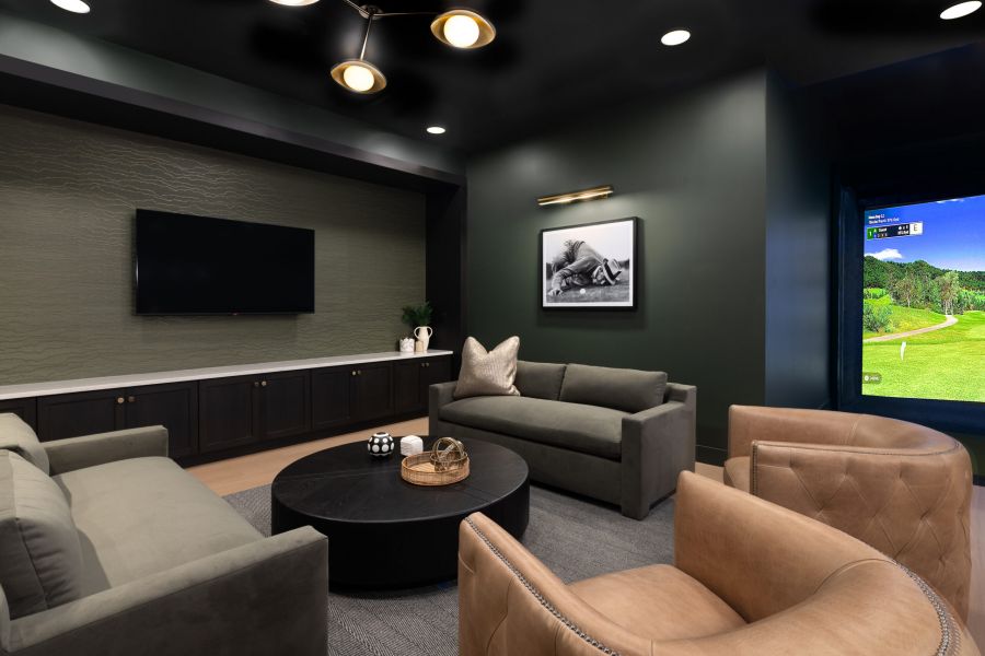 Modern lounge with sofas, armchairs, TV, and golf simulator showing a course on the right side.