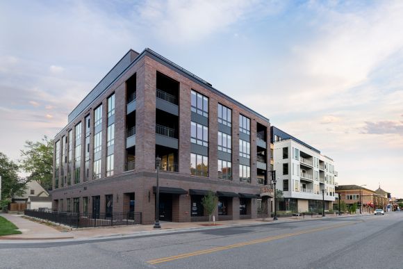 Modern brick and white apartment building on a quiet street with trees and a partly cloudy sky.
