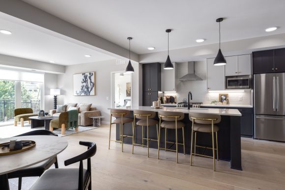 Modern open-concept kitchen and living room with island seating, pendant lights, and large windows letting in natural light.