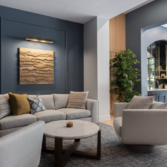 Modern living room with a gray sectional sofa, round coffee table, and wall art on a dark accent wall.