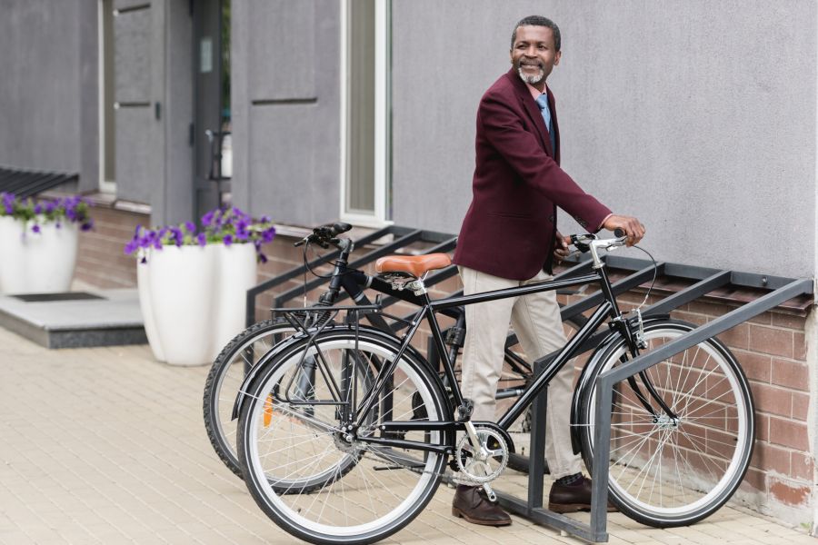 Smiling man in a maroon blazer parking his bicycle at a bike rack outside a modern building.