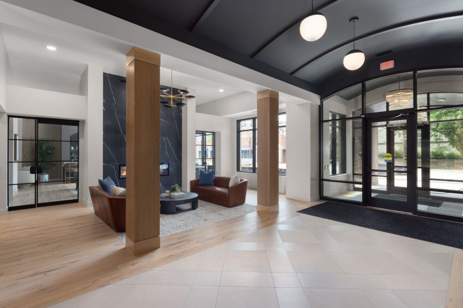 Modern lobby with leather chairs, a black accent wall, large windows, and wood and tile flooring.