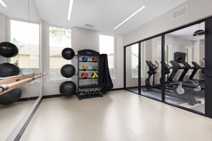 A bright gym room with exercise balls, kettlebells, mirrors, and treadmills behind a glass wall.